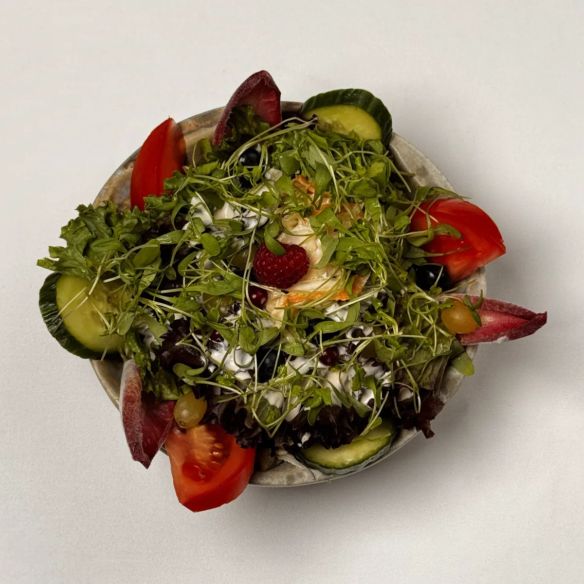 Gemischter Salat in der Schüssel mit Blattsalaten, Tomaten, Gurke, Kresse, Beeren und Hausdressing