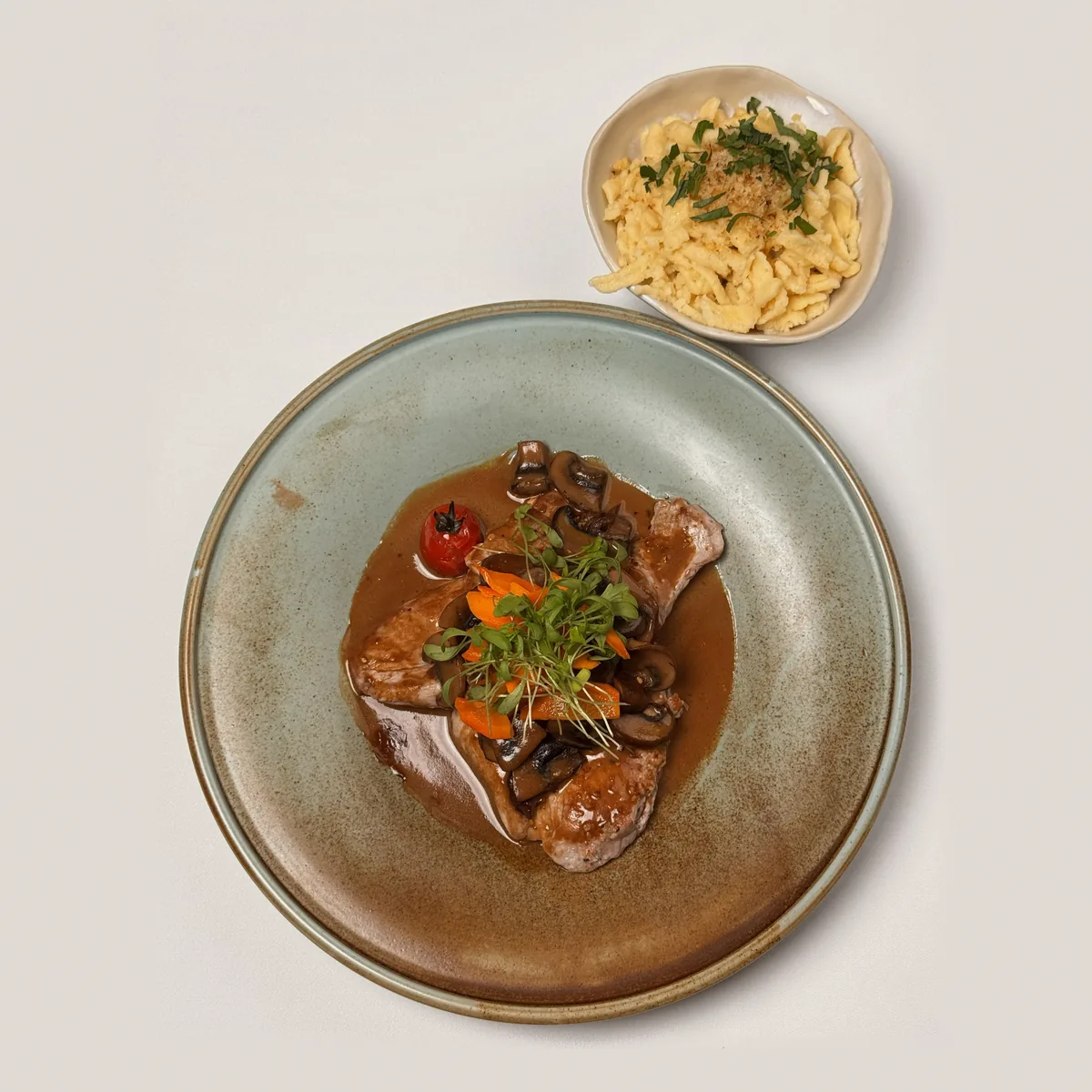Drei Medaillons vom Schweinefilet in Pilzsoße mit Champignons, Karottenstreifen und Kresse, daneben ein Schälchen geschmälzte Spätzle