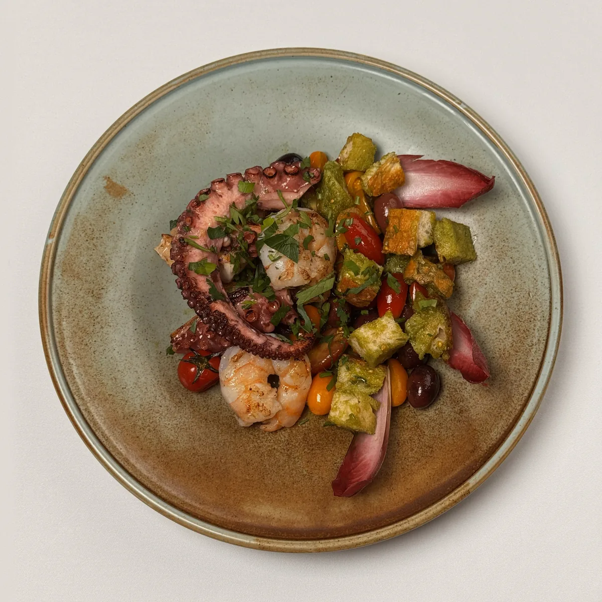 Gegrillter Pulpo und Riesengarnelen mit Brotwürfeln, bunten Kirschtomaten, Kalamata-Oliven und rotem Chicorée