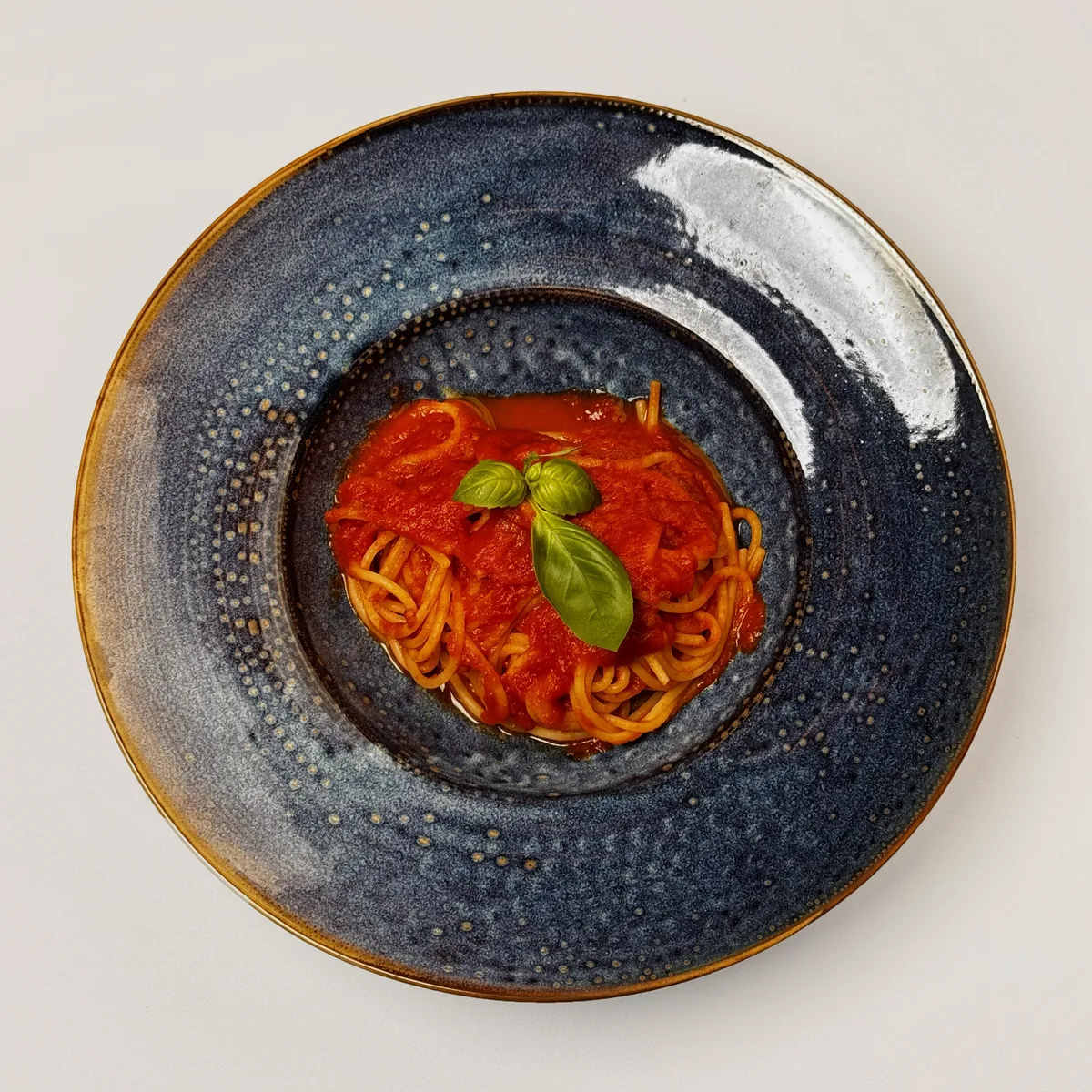 Spaghetti Napoli mit Tomatensoße und Basilikum im blauen Pastateller