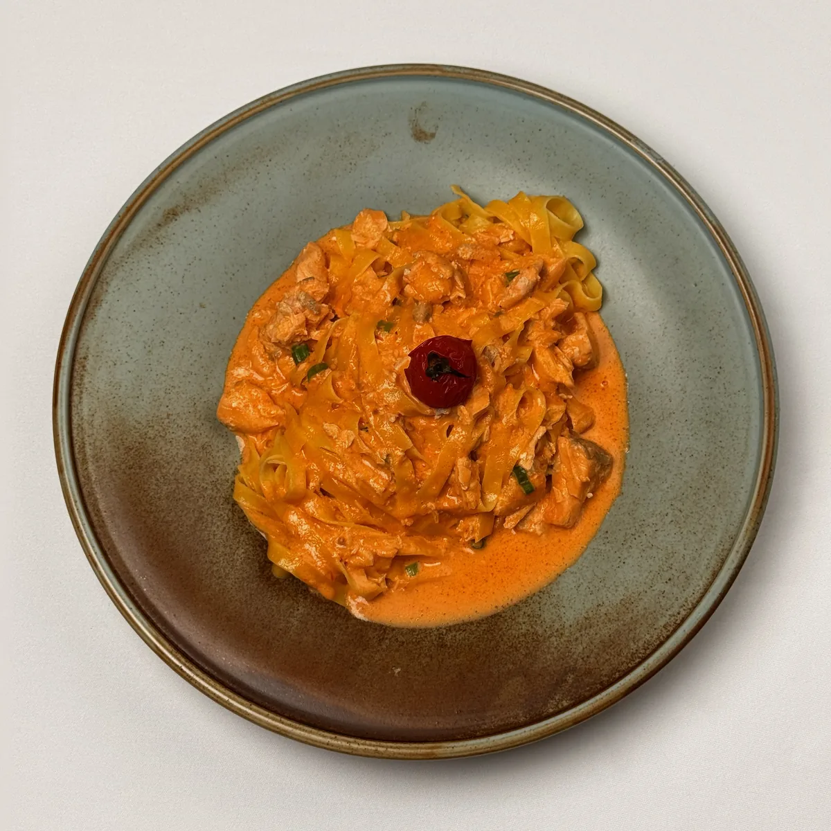 Tagliatelle al Salmone mit Lachsstücken in Tomaten-Sahnesoße, Frühlingszwiebeln und einer Kirschtomate