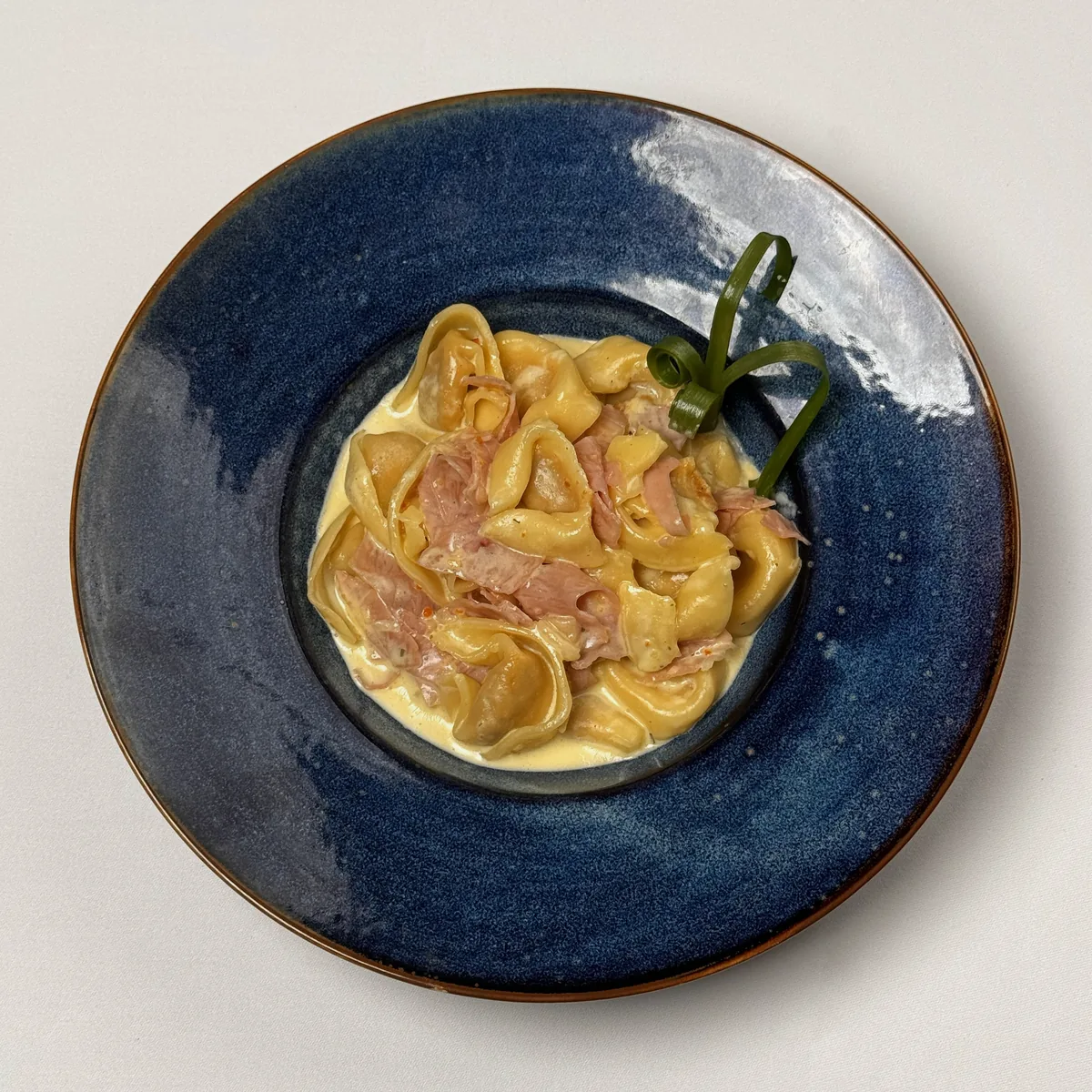 Tortellini mit Schinken in Sahnesoße im blauen Pastateller