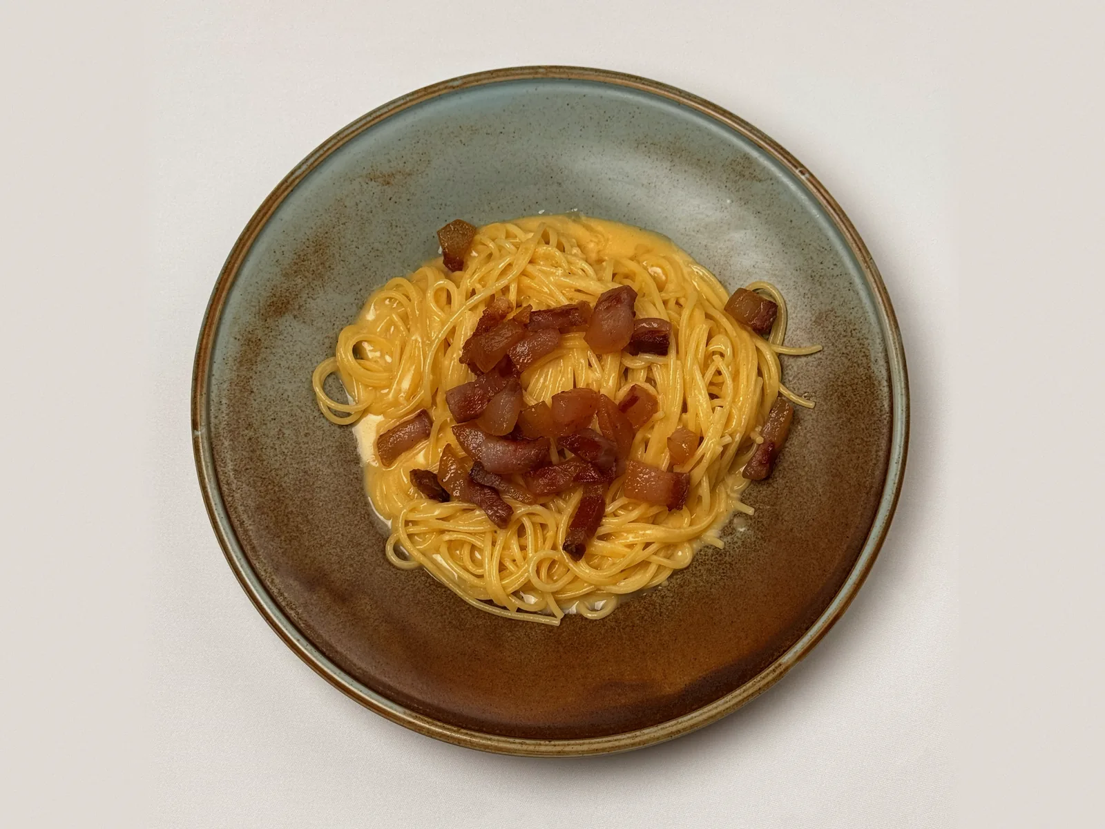 Spaghetti Carbonara mit knusprigem Guanciale auf einem graugrünen Steinzeugteller, von oben