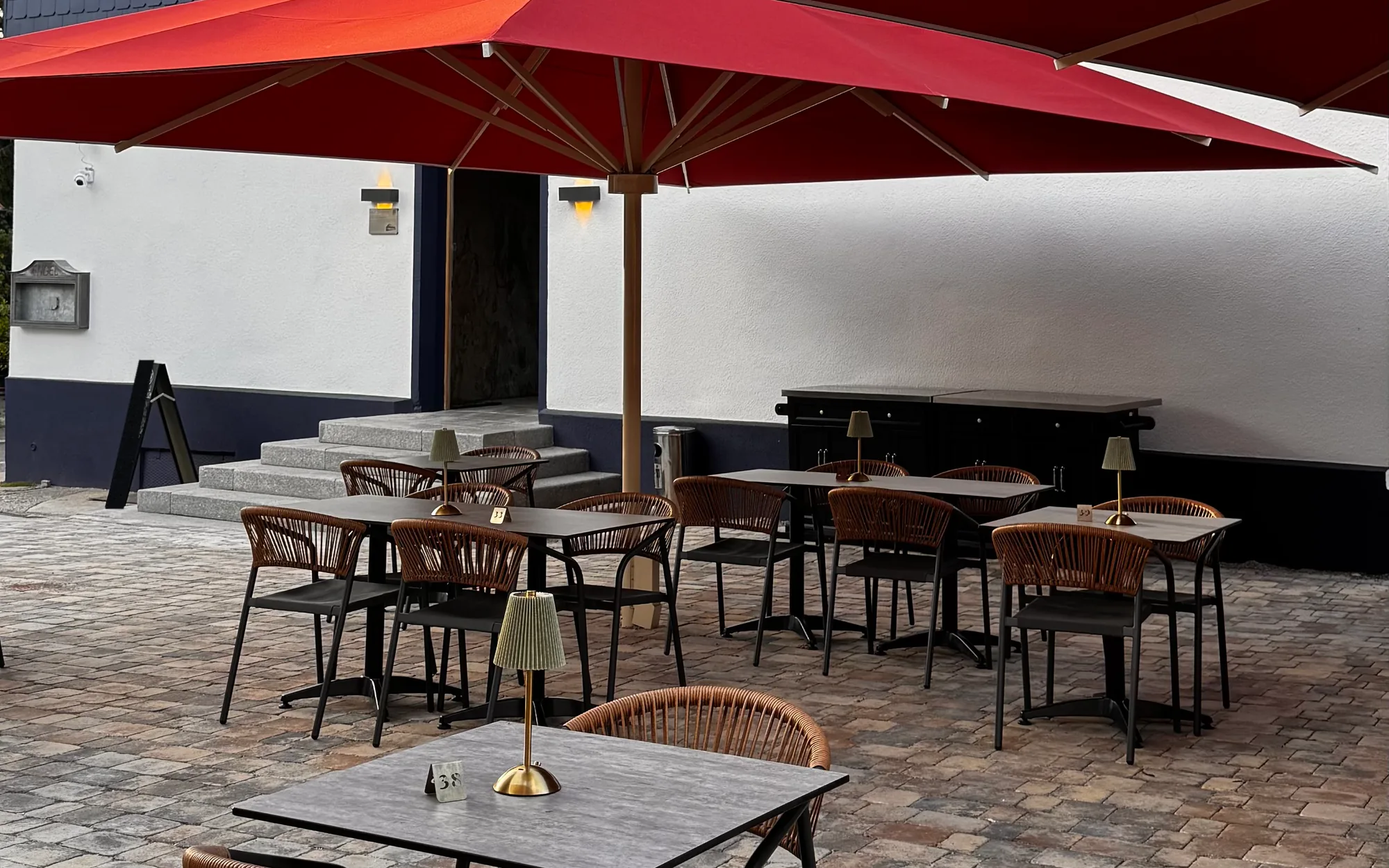 Terrasse des Landgasthofs Engel: Tische mit Flechtstühlen und Tischlampen unter großen roten Sonnenschirmen vor dem Eingang